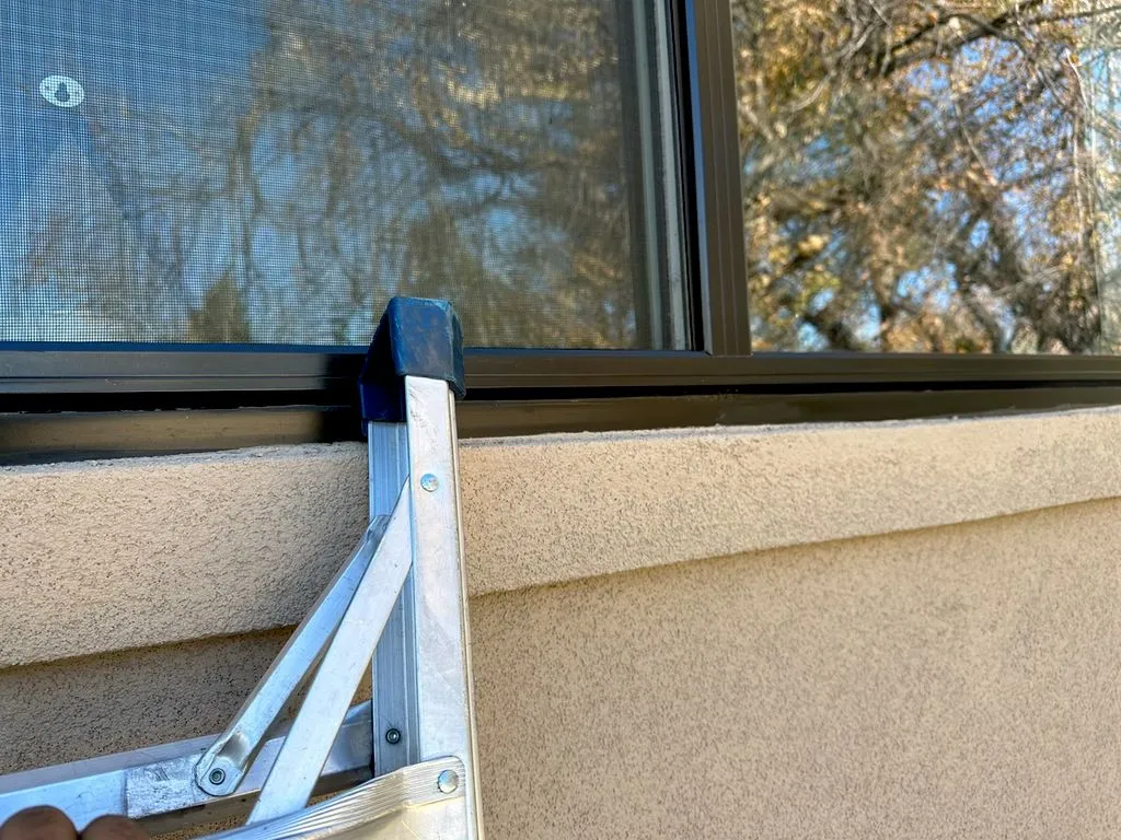 Aluminum ladder set against a stucco wall beneath a window during stucco repair work