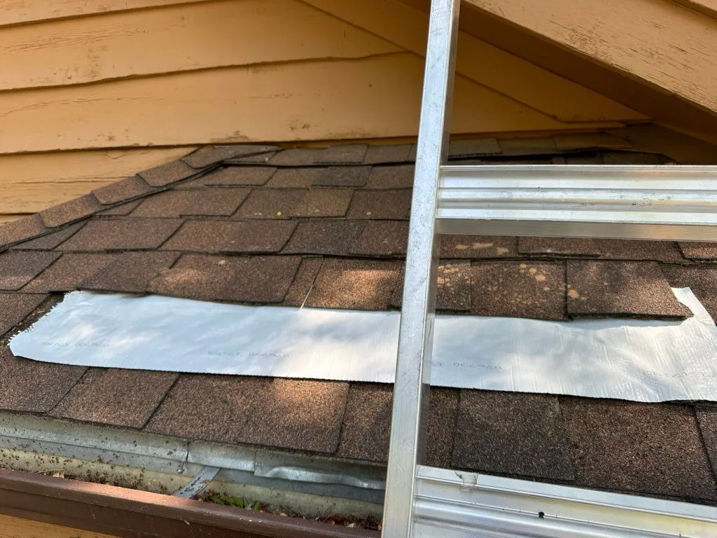 Silver repair membrane applied across worn asphalt shingles during a roof repair