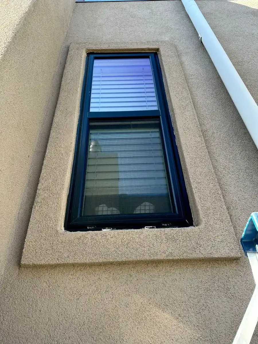 Dark-framed window surrounded by a fresh unpainted stucco patch after repair